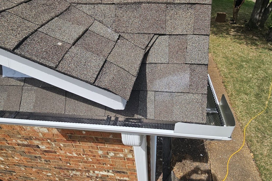 Mesh gutter guard and white downspout at the corner of a brick home