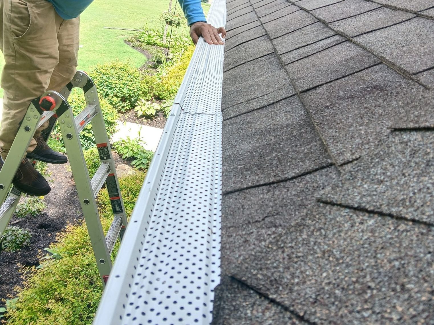 Installer fastening a perforated gutter guard along the roof edge